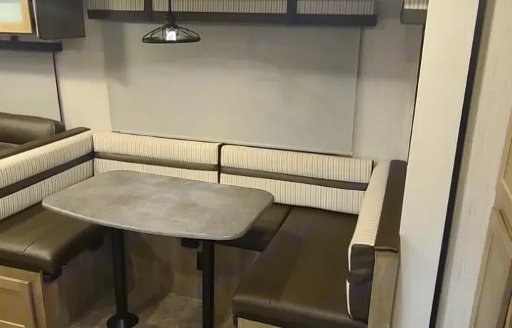 RV rental dinette with L-shaped booth seating & grey table, lit by an industrial-style light.. Palomino Puma 28DBFQ 2021