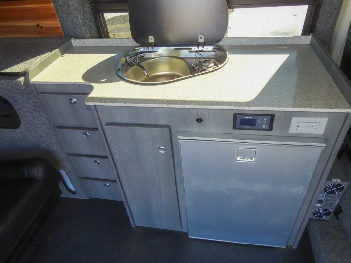 Interior of an rv rental: functional campervan kitchen with integrated sink/cooktop, Isotherm fridge, and storage.. Dodge Promaster- Summit X Edition OA9 2021
