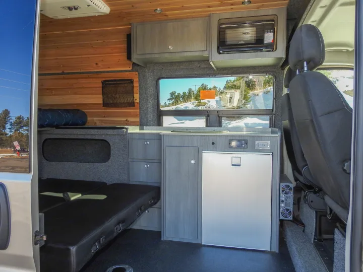 Custom rv rental interior: wood walls, full kitchen with fridge, microwave, and convertible seating/bed for trips.. Dodge Promaster- Summit X Edition OA8 2021