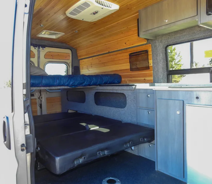 Spacious RV rental interior featuring a wood-paneled ceiling, bunk bed, and a convertible lower bed/seating area.. Dodge Promaster- Summit X Edition OA8 2021