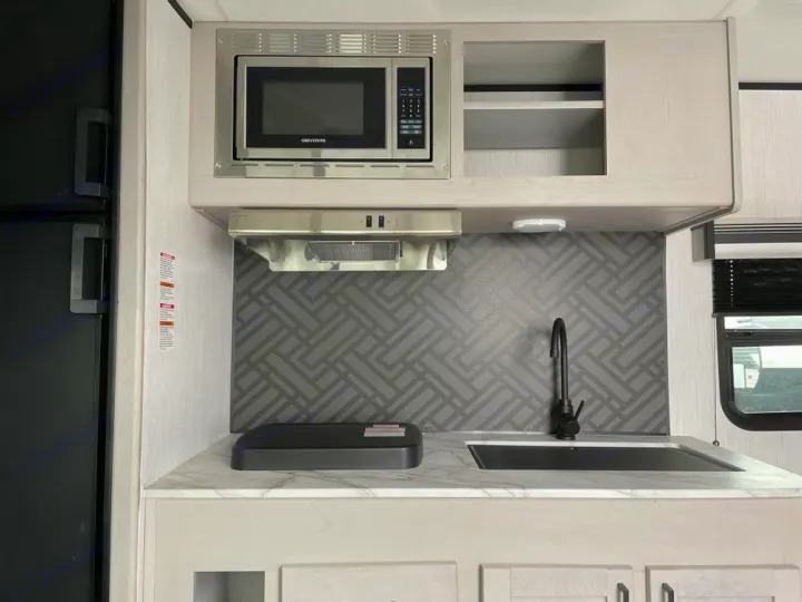 RV rental kitchen: modern compact space with black sink, microwave, refrigerator, and patterned backsplash.. Heartland Mallard 180BH 2022