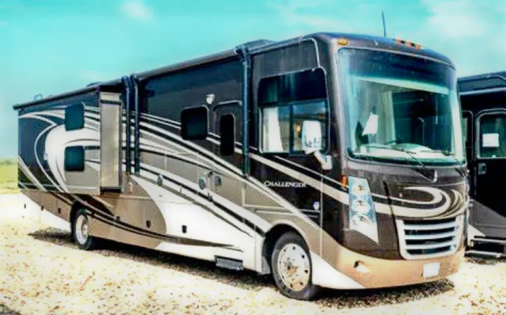 A brown and tan Class A RV with extended slide-outs, ideal for rv rental vacations. Parked on gravel under a blue sky.. Thor Challenger 2015
