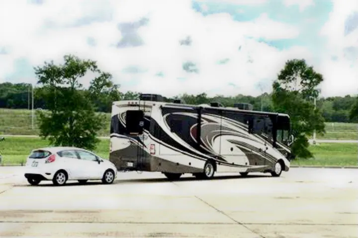 An RV rental, a large motorhome with a distinctive swirl design, is parked with its flat-towed car ready for travel.. Thor Challenger 2015
