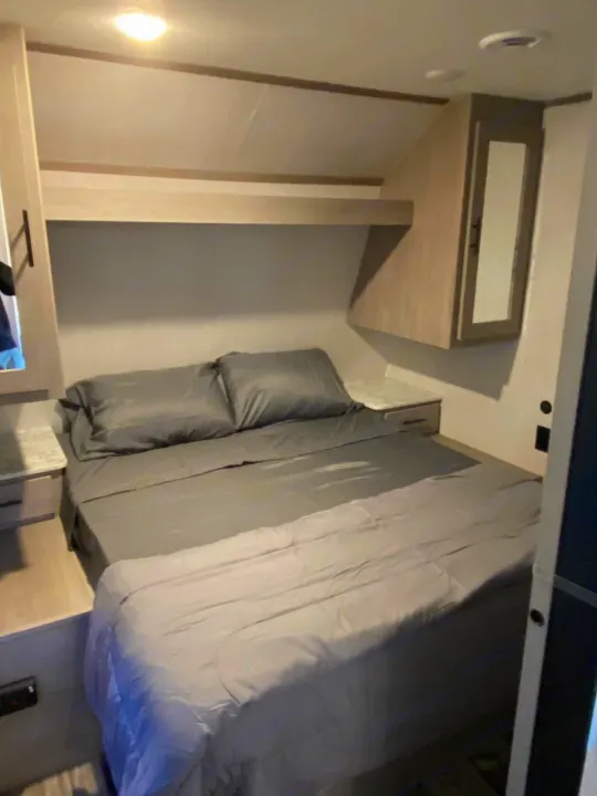 Cozy RV rental bedroom featuring a comfortable bed, bedside tables, and ample overhead storage. Ideal for road trips.. Dutchmen Coleman 2022