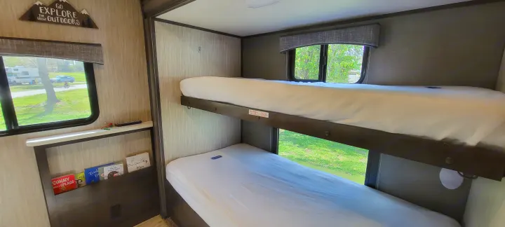 Inside an RV rental: comfy bunk beds, window views, and a 'Go Explore' sign with kids' books.. Heartland RVs Sundance 2018