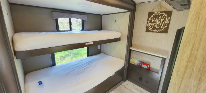 Cozy RV rental interior featuring twin bunk beds, crisp white sheets, and a window with nature views.. Heartland RVs Sundance 2018
