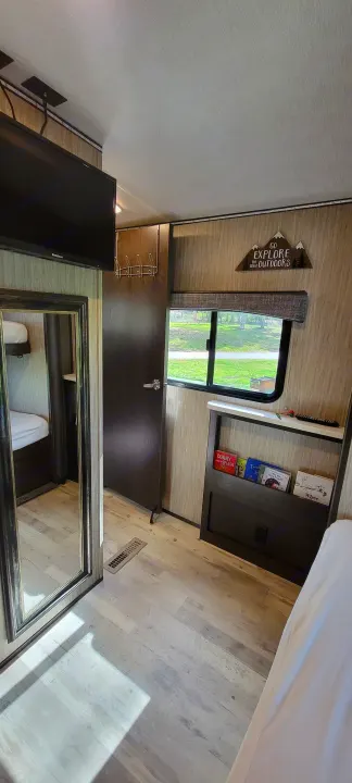 Cozy RV rental interior: bedroom area with bed, TV, mirror, and window view, inviting outdoor adventures.. Heartland RVs Sundance 2018