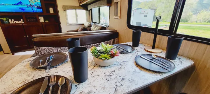 Enjoy meals in this RV rental dining nook, featuring a set table, plants, and a window view of the campground.. Heartland RVs Sundance 2018