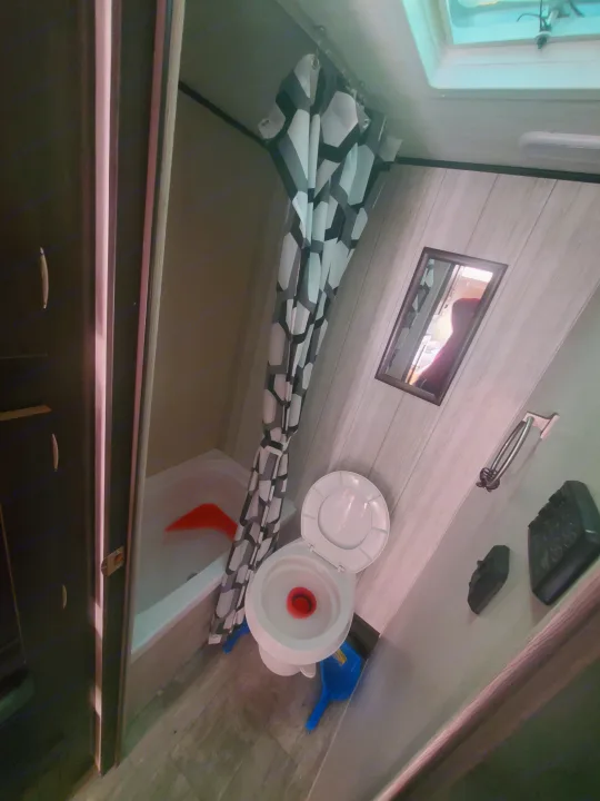 RV rental bathroom with a white toilet, shower/tub with a geometric curtain, and wooden-look interior finishes.. Heartland RVs Pioneer 2020
