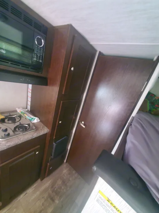 Compact RV rental interior featuring a kitchen with microwave, stove, cabinets, and a glimpse of the sleeping area.. Heartland RVs Pioneer 2020