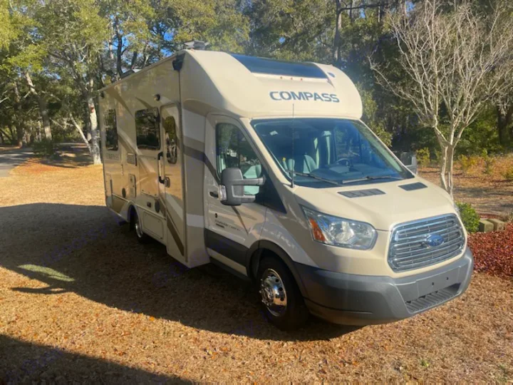 View of a tan Compass RV rental, a compact camper van on a Ford Transit chassis, parked on gravel.. Thor Compass 2016