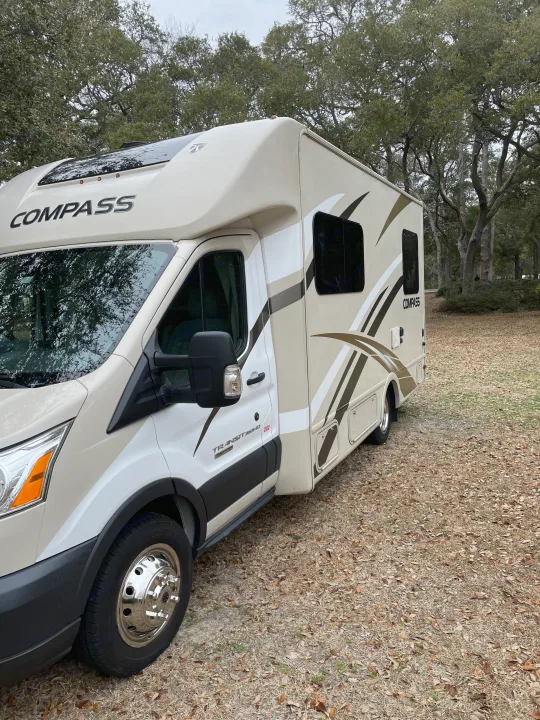 A beige and white Compass Class C RV rental, built on a Ford Transit chassis, is parked among trees.. Thor Compass 2016