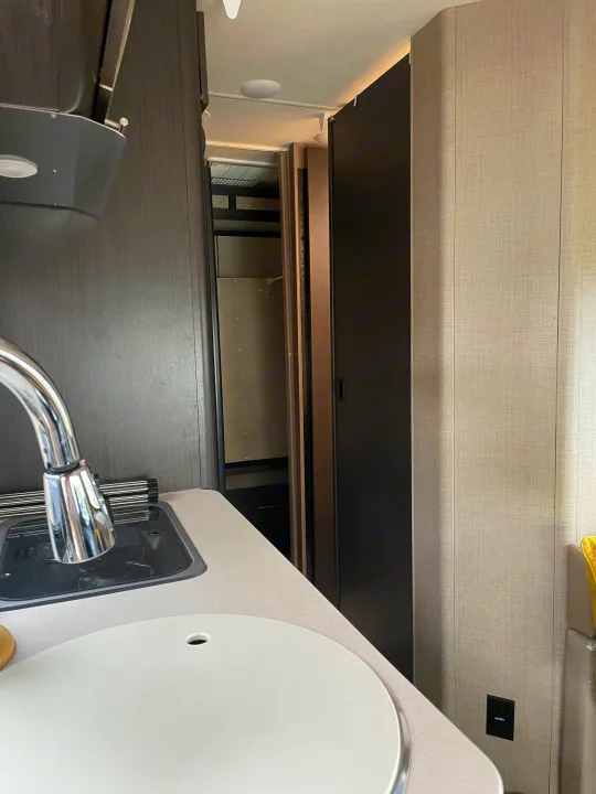 RV rental interior: galley kitchen featuring a sink, faucet, dark wood-look cabinets, and light textured walls.. Thor Compass 2016