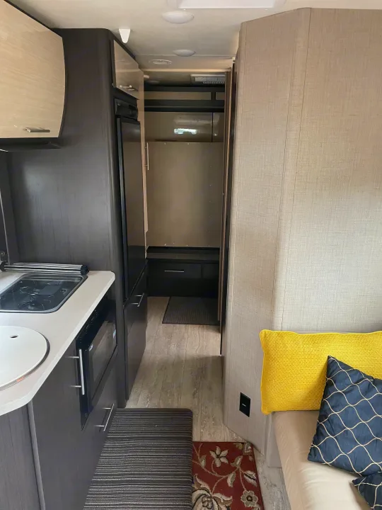 Modern RV rental interior: compact kitchen with stove & microwave, leading to a cozy living area with pillows.. Thor Compass 2016