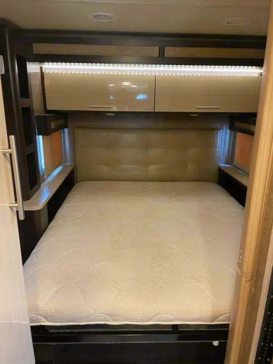 Relax in this RV rental bedroom. It features a comfortable bed, padded headboard, overhead cabinets, and bright LED lighting.. Thor Compass 2016