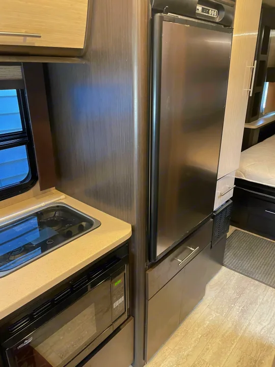 RV rental interior featuring a compact kitchen with built-in stove/sink, microwave, and a tall stainless steel refrigerator next to a bed.. Thor Compass 2016