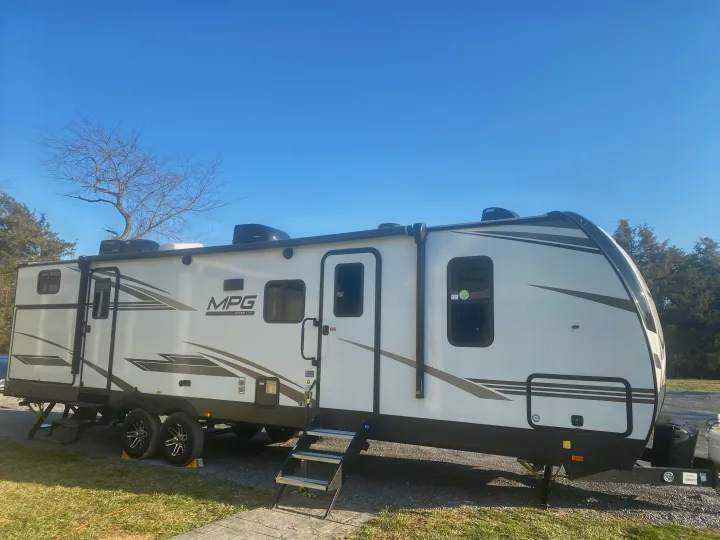 A white MPG travel trailer, perfect for an RV rental, is parked with steps down under a clear blue sky.. Cruiser RV MPG Ultra Lite 2021