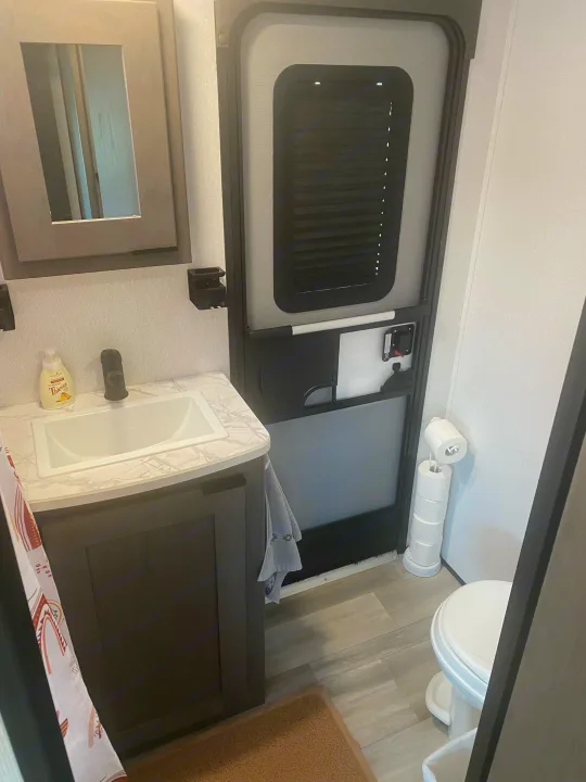 RV rental bathroom featuring a marble-look vanity, sink, mirror, compact door, and toilet with a toilet paper stand.. Cruiser RV MPG Ultra Lite 2021