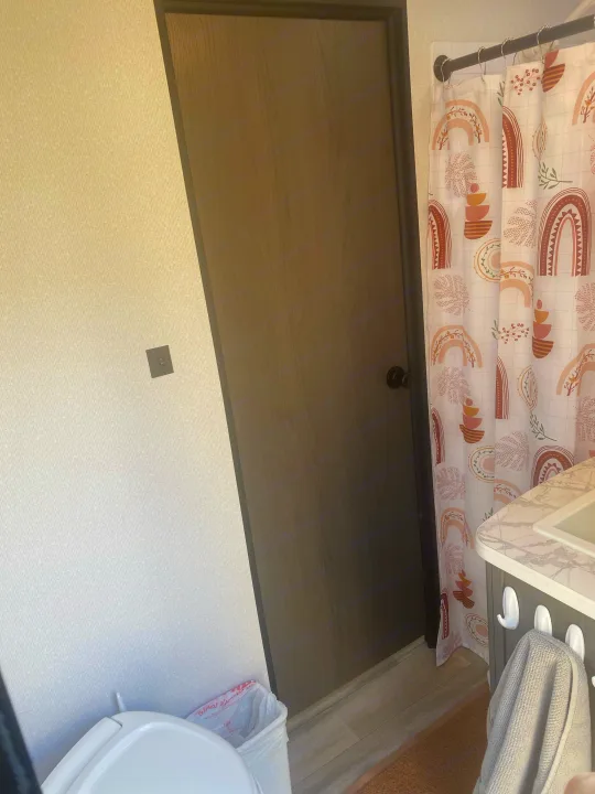 Inside a compact RV rental bathroom: toilet, door, patterned shower, and vanity with towel.. Cruiser RV MPG Ultra Lite 2021