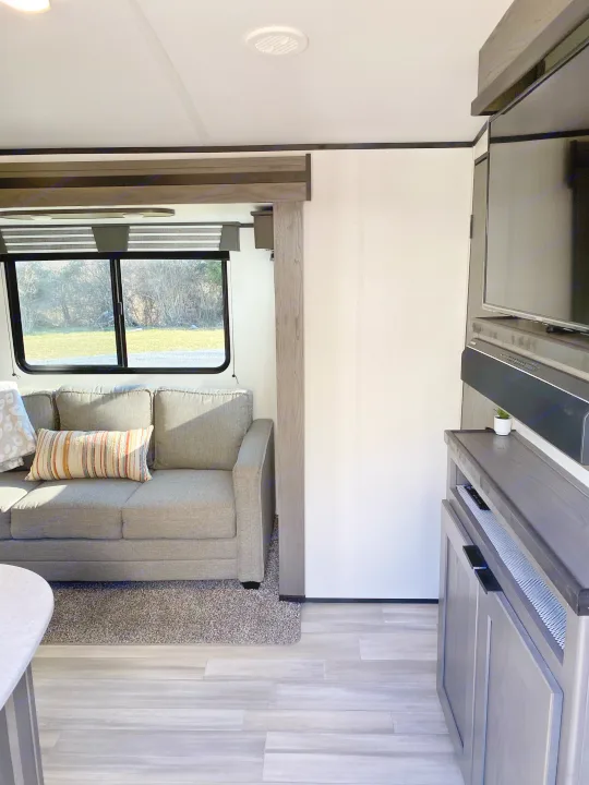 Cozy RV rental living space with gray sofa, large window, and entertainment center, perfect for relaxation.. Cruiser RV MPG Ultra Lite 2021