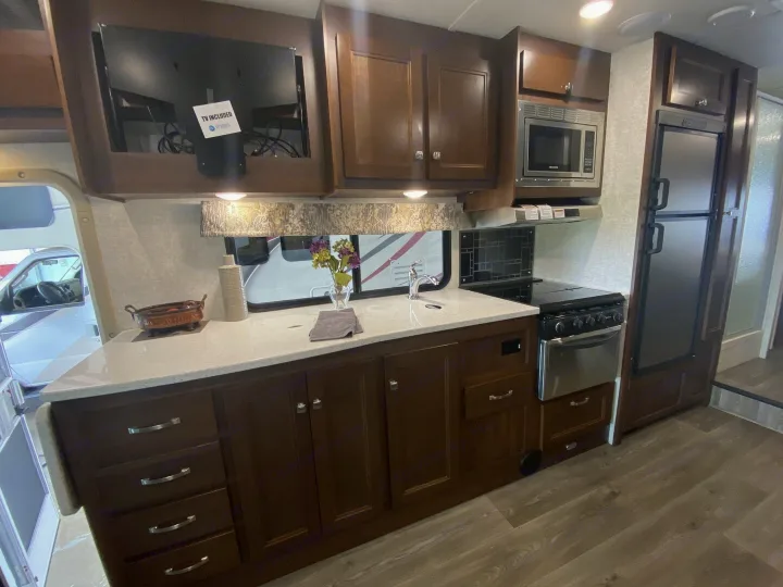 Modern RV rental kitchen interior featuring a microwave, stove, fridge, and TV. Ideal for comfortable travel and adventures on the road.. Forester Forester Motorhome 2017