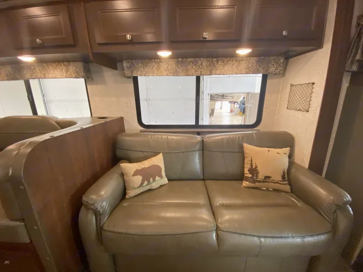 An RV rental's inviting living area shows a plush, light-colored sofa with nature-themed pillows, wood cabinets, and large windows.. Forester Forester Motorhome 2017