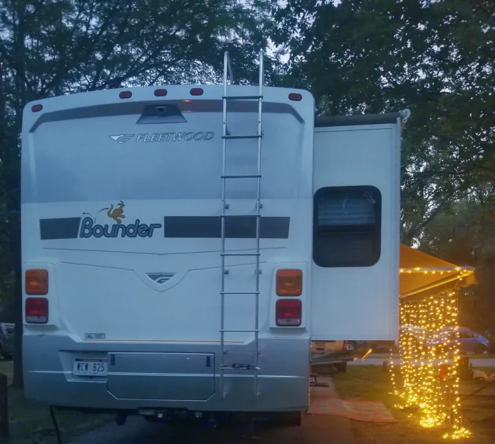 Rear of a Fleetwood Bounder RV rental, slide-out extended, illuminated by bright string lights at a pleasant campsite.. Fleetwood Other 2006