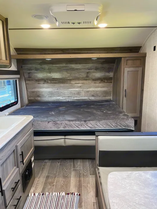 Spacious RV rental interior showing a bed with gray mattress, kitchen sink, and dinette seating.. Travel Lite Superlite 2022