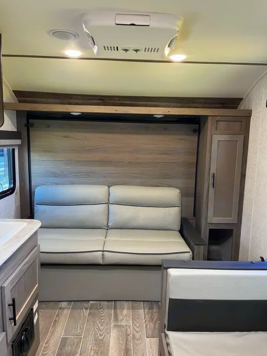 Cozy rv rental interior featuring a convertible sofa, modern wood-look flooring, overhead AC, and integrated storage. Perfect for travel.. Travel Lite Superlite 2022