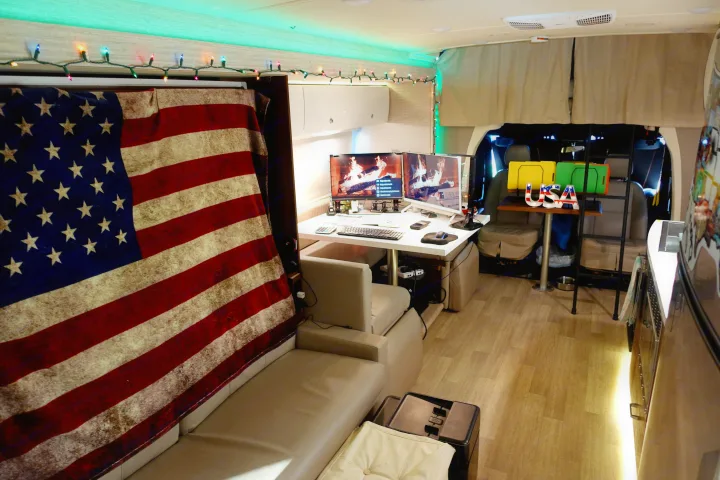 Inside a unique RV rental: a cozy mobile office with multi-monitor workstation, American flag, and festive string lights.. Winnebago Navion 2020