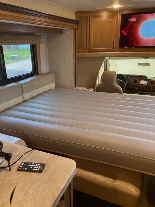 RV rental interior: A spacious inflatable bed fills the main living area, with the driver's cockpit and a mounted TV in view.. Gulf Stream B Touring Cruiser 2019