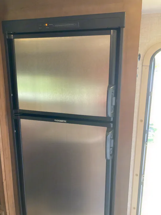 A Dometic two-door stainless steel refrigerator and freezer unit in an rv rental, with an illuminated control panel.. Gulf Stream B Touring Cruiser 2019