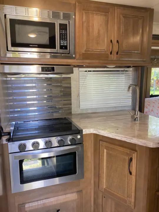 Modern RV rental kitchen featuring a Greystone microwave, stove, oven, and sink with ample counter space.. Gulf Stream B Touring Cruiser 2019