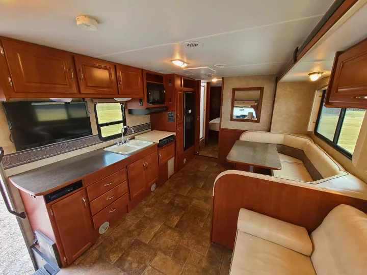 Spacious RV rental interior featuring a well-equipped kitchen, dining dinette, and living space with TV.. Winnebago Minnie Winnie 2014