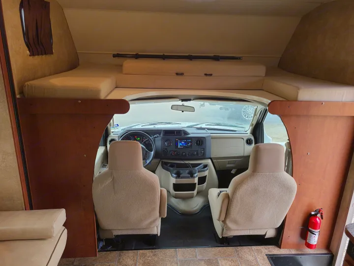 View inside an RV rental showing the cockpit with dashboard & front seats, an over-cab bunk, and a fire extinguisher.. Winnebago Minnie Winnie 2014