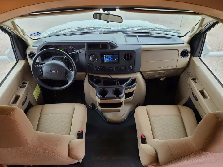 Spacious RV rental cabin interior with dashboard, steering wheel, and passenger seating, viewed through a frosted windshield.. Winnebago Minnie Winnie 2014