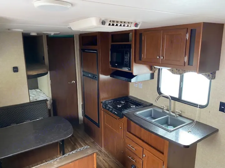 RV rental interior: cozy kitchen with sink & stove, dining area, bunk beds, and refrigerator.. prowler lynx 22LX 2015