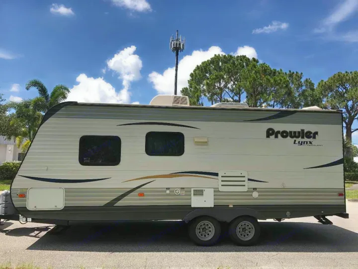 Light-colored Prowler Lynx travel trailer for rv rental. Two-axle camper parked outdoors under a blue sky.. prowler lynx 22LX 2015