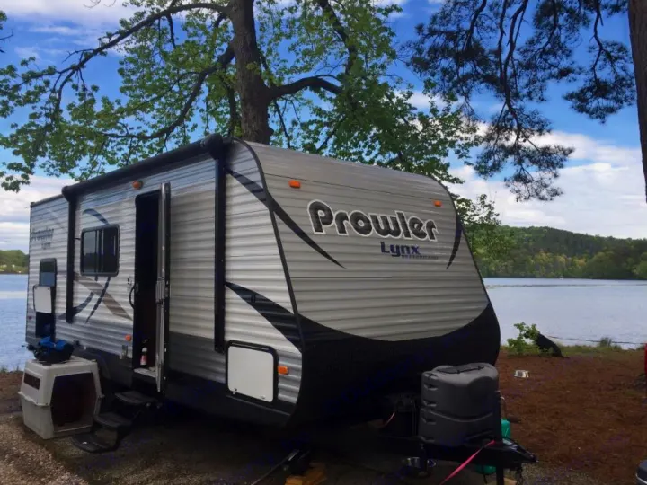 An RV rental, a Prowler Lynx travel trailer, is set up at a scenic lakeside campsite under a blue sky.. prowler lynx 22LX 2015
