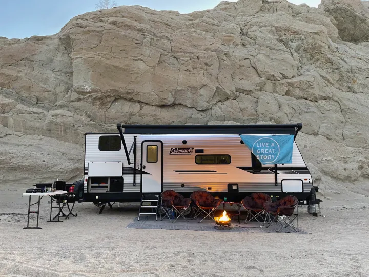 Enjoying the outdoors! This Coleman **rv rental** offers desert camping with a cozy campfire and chairs by impressive rock cliffs.. Coleman Lantern 2022
