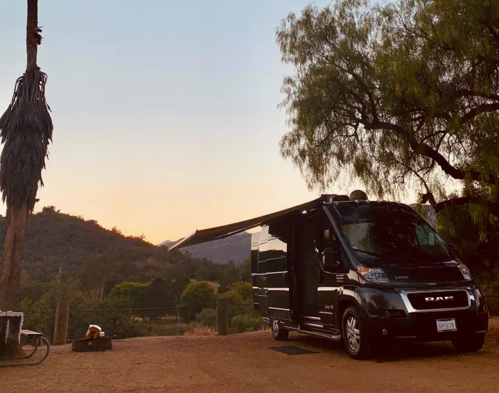 Enjoying a beautiful sunset at a scenic campsite with an extended awning from a black rv rental camper van, ready for adventure.. Pleasure-Way Pleasure-Way Class B 2020