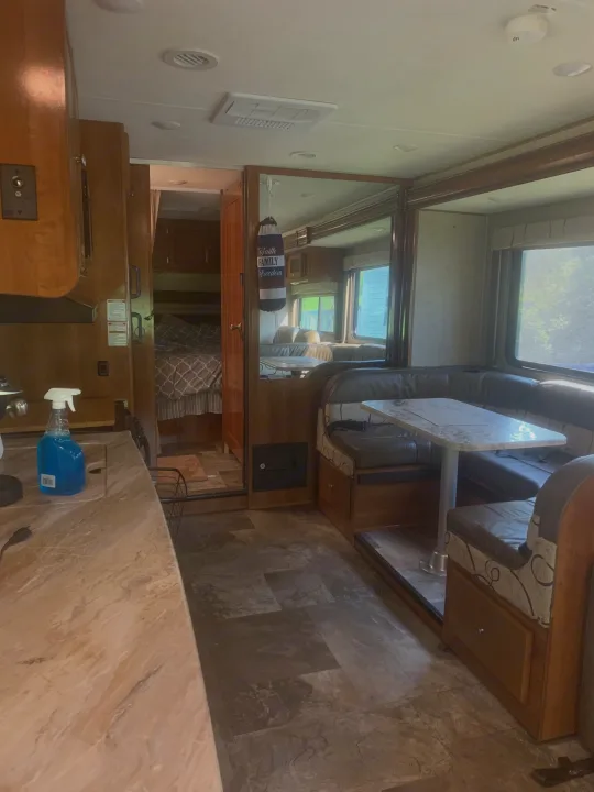 RV rental interior showcasing a kitchen counter, dining booth, and a peek into the cozy bedroom. Ready for adventures!. Forest River Coachmen Leprechaun 2018