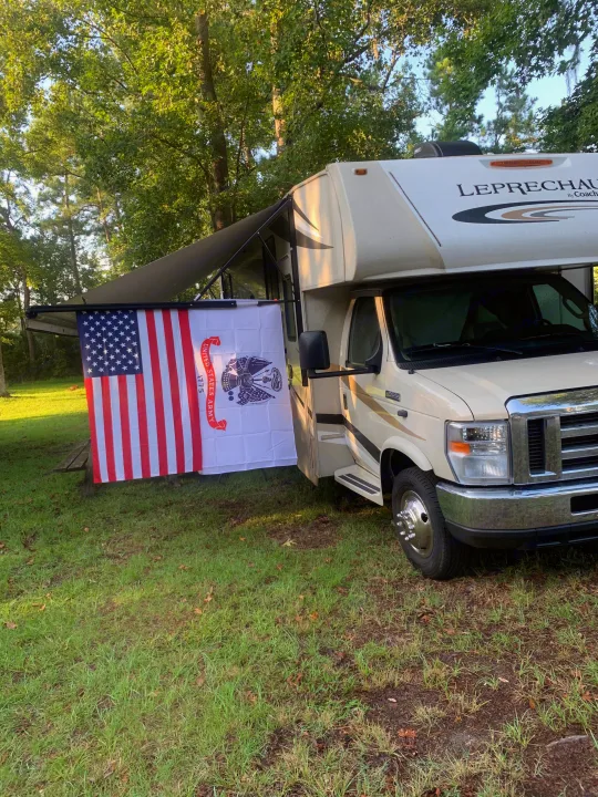 RV rental parked at a campsite, featuring an American flag and U.S. Army flag proudly displayed from the awning.. Forest River Coachmen Leprechaun 2018