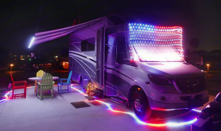 A bright rv rental adorned with patriotic and colorful lights, an extended awning, and a cozy patio setup for nighttime enjoyment.. Winnebago Navion 2020