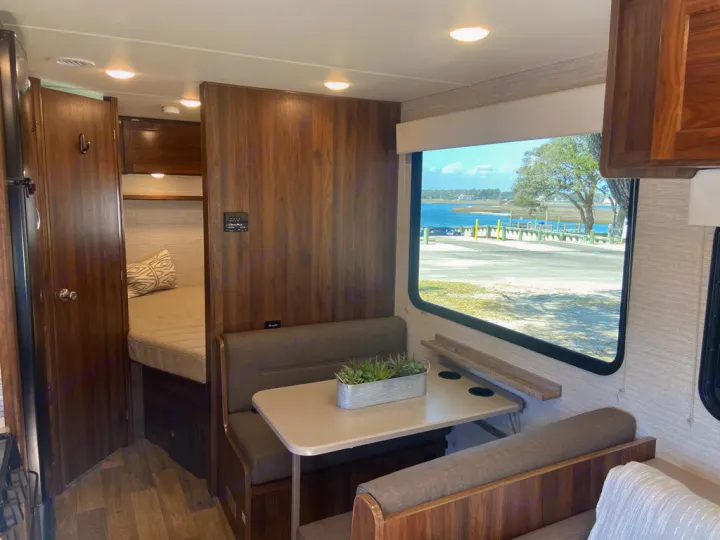 RV rental interior with a cozy dinette, sleeping area, and a beautiful window view of water and a dock.. Winnebago Outlook 2020