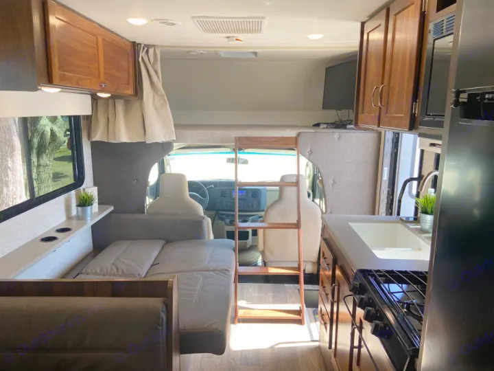RV rental interior view: compact kitchen, convertible dinette/bed, overhead bunk, and storage for travel.. Winnebago Outlook 2020