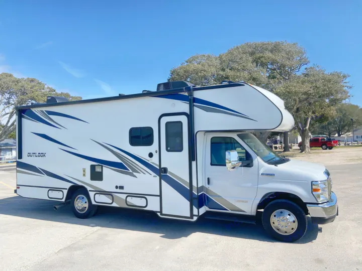 A white and blue 'Outlook' Class C motorhome, ready for adventure. This spacious RV rental is parked outdoors under a clear sky.. Winnebago Outlook 2020