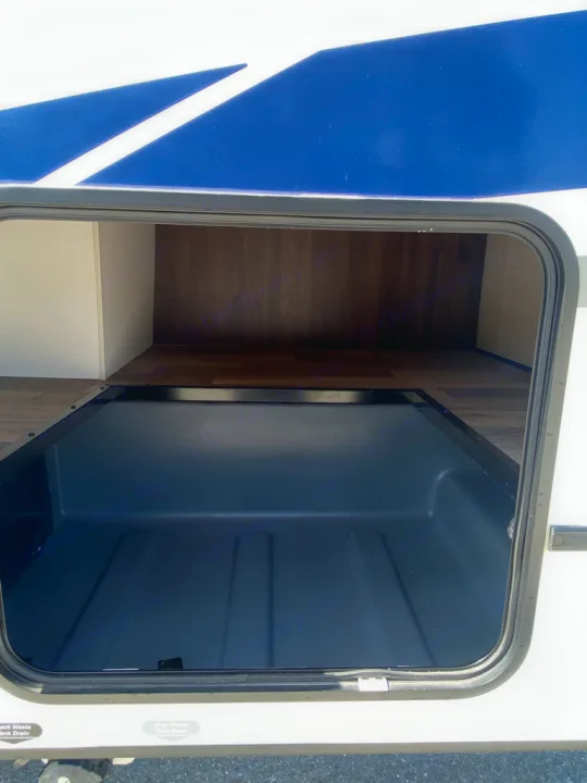 Spacious exterior storage in an RV rental, perfect for camping gear. The compartment has a durable gray floor and wooden walls.. Winnebago Outlook 2020
