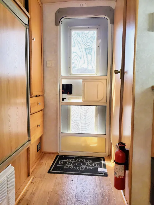 Inside an RV rental: welcoming entrance with a screen door, safety extinguisher, and functional cabinetry on the left.. R-Vision T-lite 2003