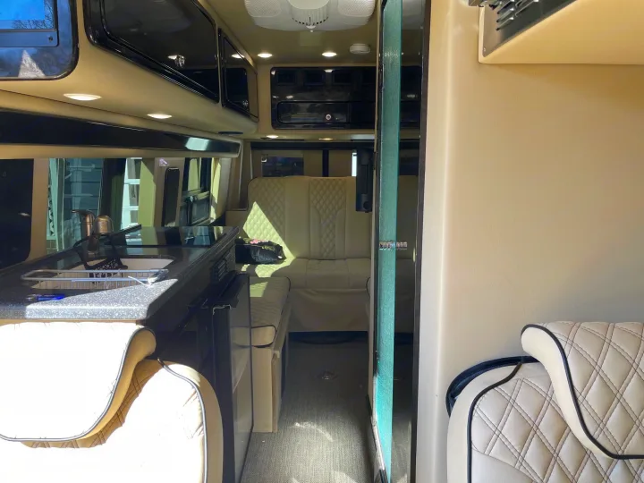 Luxury RV rental interior featuring a modern kitchen area, plush quilted seating, and sleek overhead cabinets, ideal for comfortable travel.. Midwest Automotive Designs Midwest Automotive Designs Class B 2020